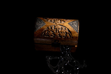 carved walnut wood box with jewels protruding from the inside illuminated from the side on a black...