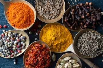 Set of spices in brass spoons, closeup, top view. Various peppers, cardamom, carnation, turmeric, paprika and saffron for cooking