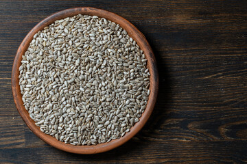 Grey raw sunflower seeds in ceramic bowl on a wooden background, closeup, top view. Purified seeds of sunflower