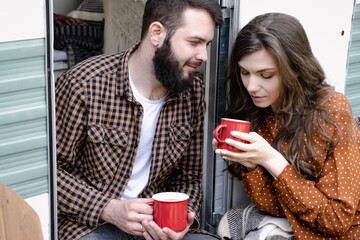 Young caucasian couple is traveling in travel van. Romantic atmosphere of relaxation. Road trip around country for the weekend. Man and woman sitting in camper and drinking tea. Millennial generation