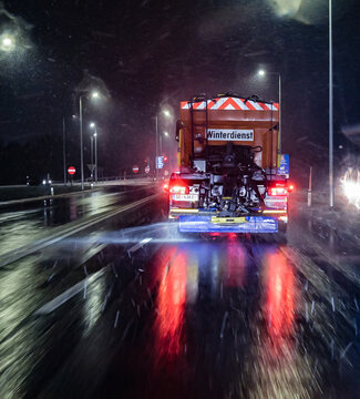 Ein Winterdienstfahrzeug verteilt Streusalz auf dem mit frisch gefallenem Schnee bedeckten Asphalt