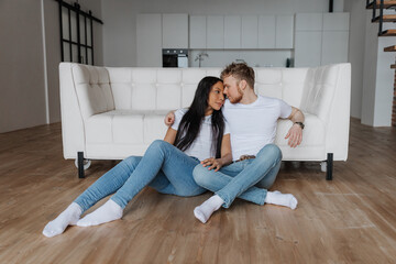 Young happy couple sitting on the floor at home and looking on each other 