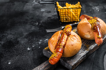 Deutsche Bockwurst sausage in a bun with French fries and curry sauce, currywurst. Black...