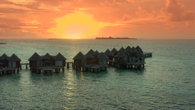 Overwater villas at the time amazing sunset in tropical sea with coral reef. Aerial drone view.