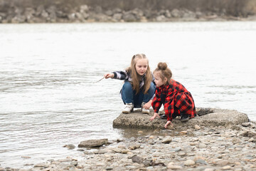 two younger sisters dressed in patterned plaid clothes have fun playing by the river
