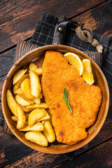 Austrian fried weiner schnitzel with potato wedges in a wooden plate. Wooden background. Top view