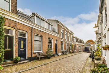 an old street in the netherlands with brick buildings and green plants on either side, there is a blue sky - obrazy, fototapety, plakaty