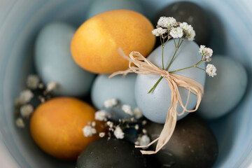 Baby blue, yellow and dark grey Easter eggs in a bowl, top view closeup. Festive decoration.