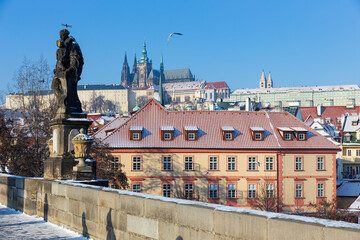 Fototapeta na wymiar Sunny snowy Prague Lesser Town with gothic Castle from Charles Bridge and its baroque Statues, Czech republic
