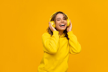 smiling attractive woman listening to music in headphones on yellow background