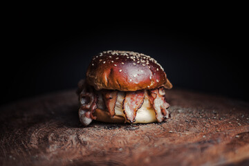 
Tasty beef, cheese, burger with many slices of bacon, warm coming out of smoke on a wooden cutting board on a black background, 
with fire on the stage. 