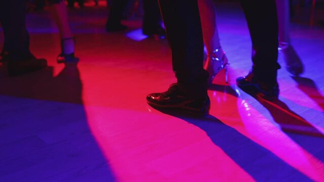 Dancing shoes of a couple, couples dancing traditional latin argentinian dance milonga in the ballroom, tango salsa bachata kizomba lesson, festival on a wooden floor, purple, red and violet lights
