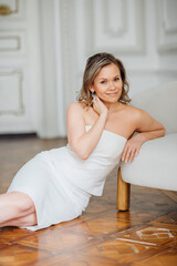 a delicate middle-aged woman in a white dress on the floor by the chair