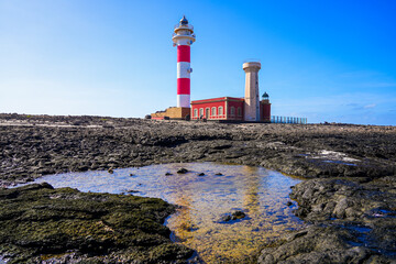 Seawater pool visible at low tide in the rocks below the red and white striped tower of the El Toston lighthouse