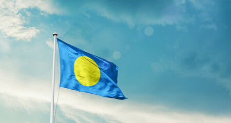 Waving Flag of Palau in Blue Sky. The symbol of the state on wavy cotton fabric.