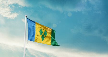 Waving Flag of Saint Vincent and the Grenadines in Blue Sky. The symbol of the state on wavy cotton fabric.
