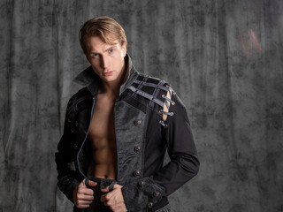 An attractive young man in a fantasy camisole, posing in the studio on a gray fabric background.