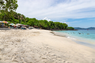Fototapeta na wymiar BALI, INDONESIA - NOVEMBER 6, 2022: Bias Tugel beach at the south of Bali island. Many tourists swimming in blue ocean water. White sand and rock shore.