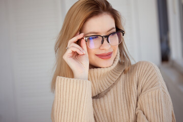 Young cute blonde with eyeglasses and a beige sweater. Stylish fashionable young woman. woman with...