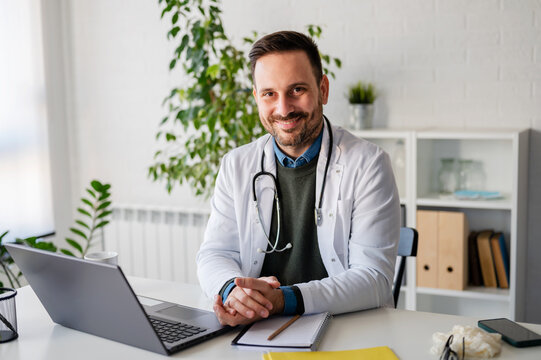 Portrait of a smiling handsome doctor sitting in his office at clinic