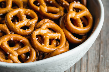 Mini pretzels with salt in a bowl on wooden background, close up.