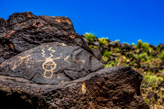 Petroglyphs on volcanic rock with sagebrush in Piedras Marcadas Canyon, Petroglyph National Monument on a sunny, spring afternoon; Albuquerque, New Mexico, United States of America