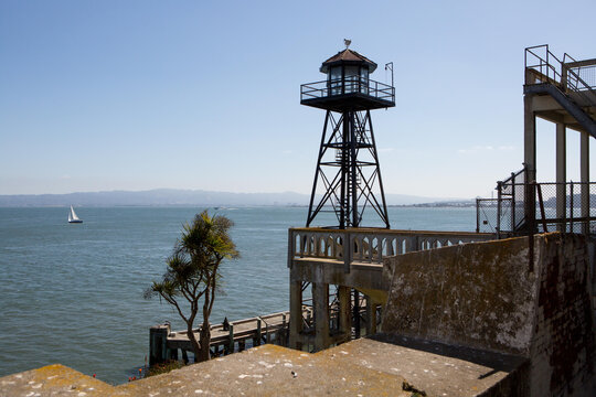 A watchtower on Alcatraz Island, and a scenic view of the water and a sailboat off shore.; Alcatraz Federal Penitentiary, Alcatraz Island, San Francisco Bay, California