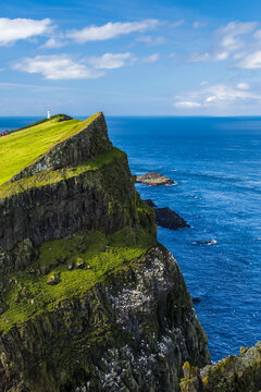 A distant lighthouse on a green cliff overlooks the Atlantic Ocean.