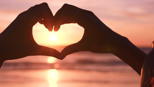 Beach, sunset and heart shape hands for love in sunshine, peace and calm relaxation for holiday travel, summer vacation or adventure. Ocean, red sky horizon and heart hands emoji with sunny landscape