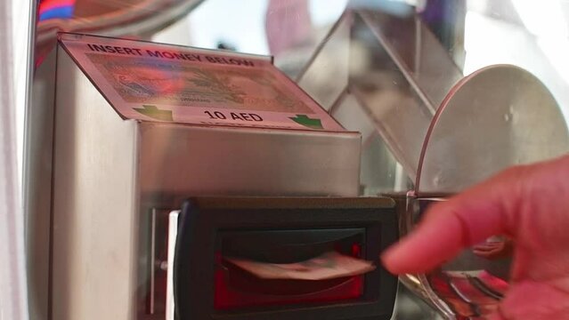 Dubai, UAE - 14th october, 2022: close up tourist put 10 AED currency notes to coin machine to print memorable gift coin in Dubai frame famous landmark