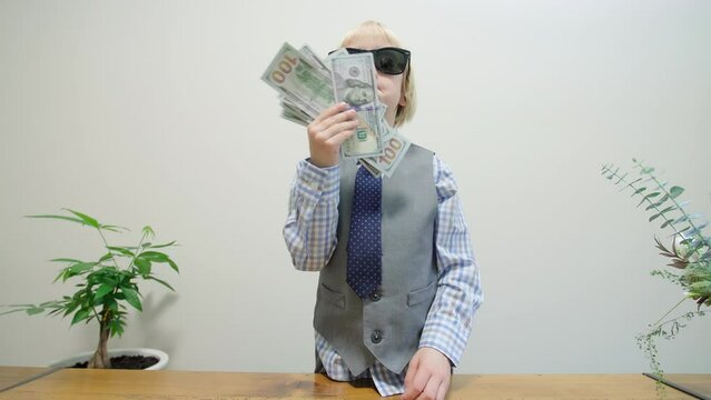 Artistic caucaisn boy in shirt, tie and sunglasses, pretending to be a rich businessman using banknotes like a fan and throwing them in the air. Little boss concept