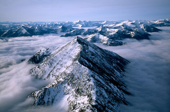 Aerial view of Montana's Rocky Mountain Front, with snowy Rocky Mountains peaks above the clouds; Montana, United States of America - Powered by Adobe