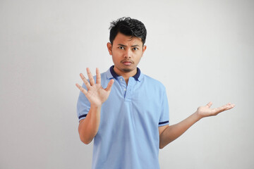 Attractive Asian man with hand gesture pose rejection or prohibition while pointing to copy space by his side wearing blue t shirt isolated on white background