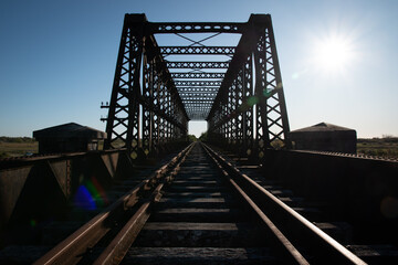 Puente ferroviario sobre vías en atardecer.