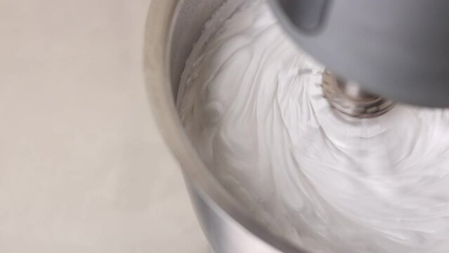 Kitchen mixer is beating the eggs white egg whites into a thick white foam. whisks whipped egg whites and sugar in the metal bowl. Whip the egg white: cook at home, make a cake, desserts, meringue