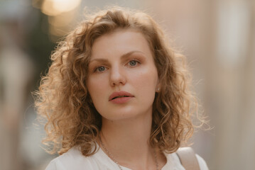 A headshot photo of a woman with curly hair in an old European town