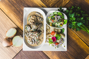 High angle shot of tasty sirloin in thick mushroom sauce served on white plate along with potato dumplings and salad. Nutrition concept. High quality photo