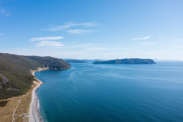 Obraz premium Beautiful aerial photograph of the sea coast. Top view of the coast and the mountainous island. Blue water and sky. Nature of Siberia and the Russian Far East. Sea of Okhotsk, Magadan region, Russia.