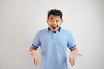 shock asian man with open hands and mouth wearing blue t shirt isolated on white background