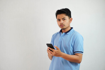 young asian man standing holding a phone with an angry and disapproving expression wearing blue t shirt isolated on white background