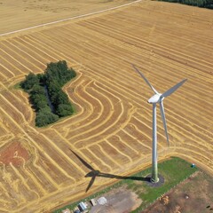 An aerial shot of a huge windmill in Europe against a brown agricultural field. A windmill generates wind energy. Wind energy. Windmill from a bird's eye view.