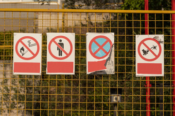 Forbidding red signs indicating danger hang on a mesh metal fence. Warning signs on the construction site. Symbols meaning danger.