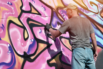 Young caucasian male graffiti artist drawing big street art painting in blue and pink tones....