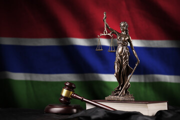 Gambia flag with statue of lady justice, constitution and judge hammer on black drapery. Concept of...