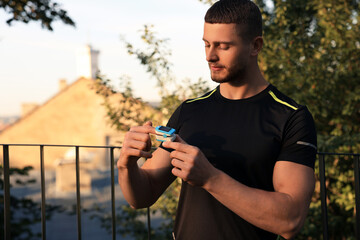 Attractive man checking pulse with blood pressure monitor on finger after training in park. Space for text