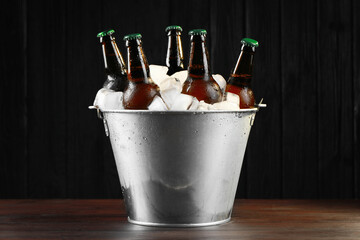 Metal bucket with bottles of beer and ice cubes on wooden table - obrazy, fototapety, plakaty