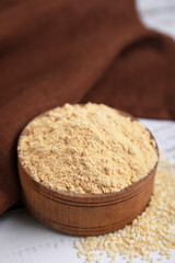 Sesame flour in wooden bowl on white table, closeup