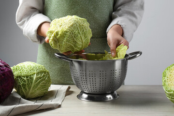 Woman putting leaf from fresh savoy cabbage at wooden table, closeup - obrazy, fototapety, plakaty