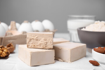 Blocks of compressed yeast and ingredients for dough on white table, closeup