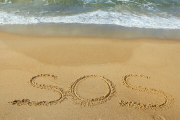 Fototapeta na wymiar Message SOS drawn on sand near wavy sea